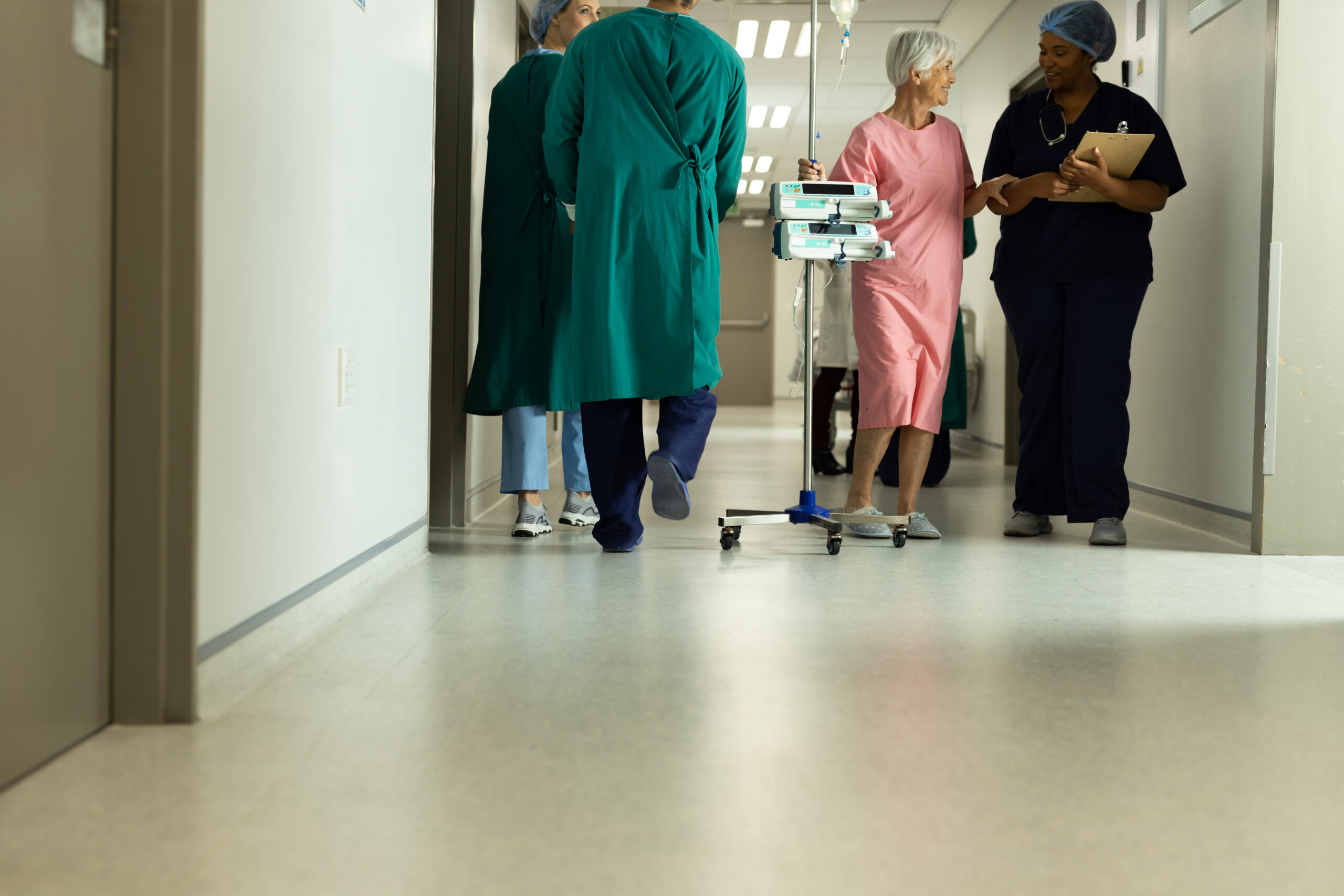 Diverse female doctor and caucasian senior female patient with iv pole talking in hospital. Hospital, medical and healthcare services, copy space. Commercial Space Epoxy Floor
