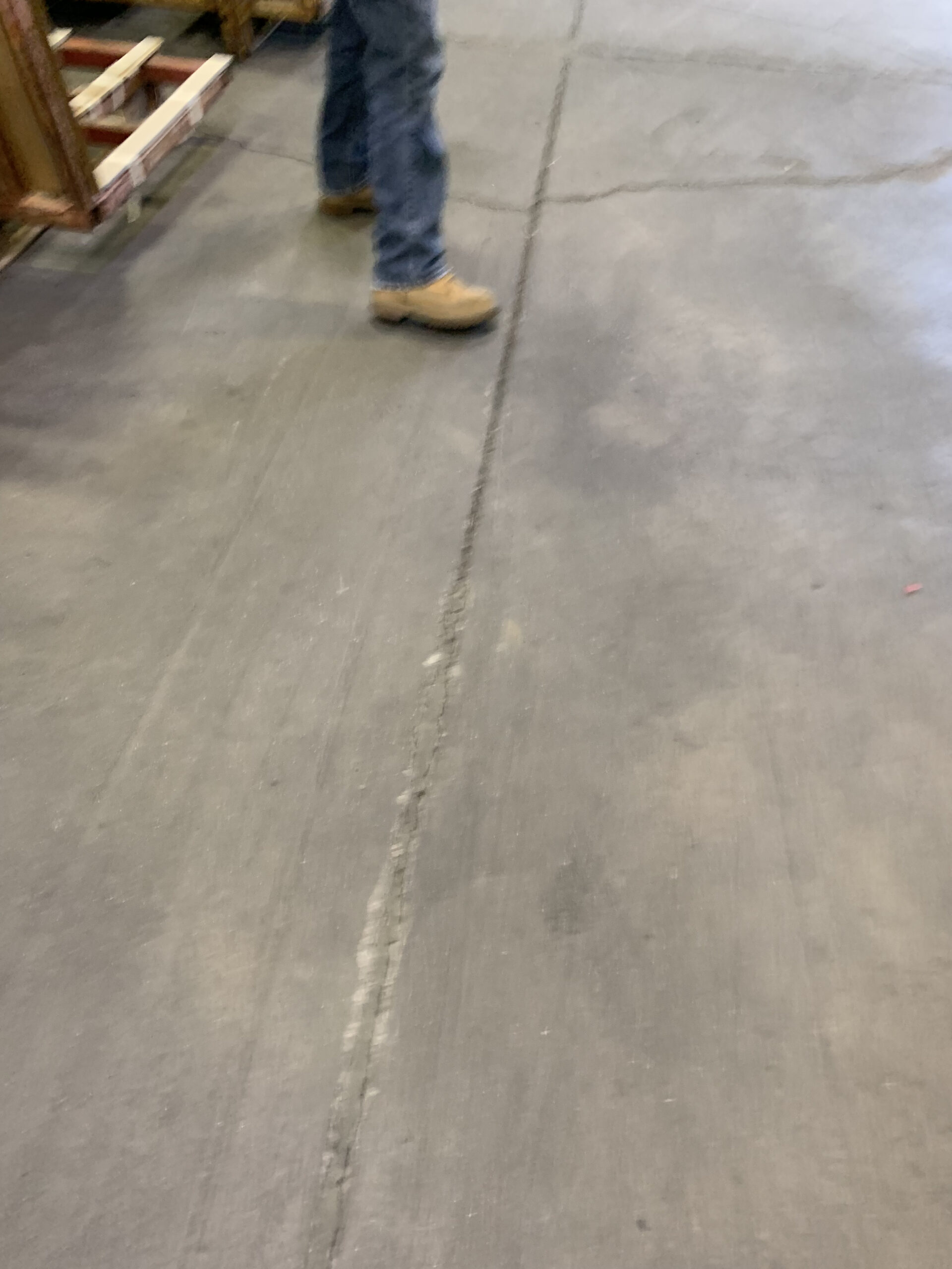 A close-up of a damaged concrete floor with a person standing nearby. — concrete floor damage warning signs