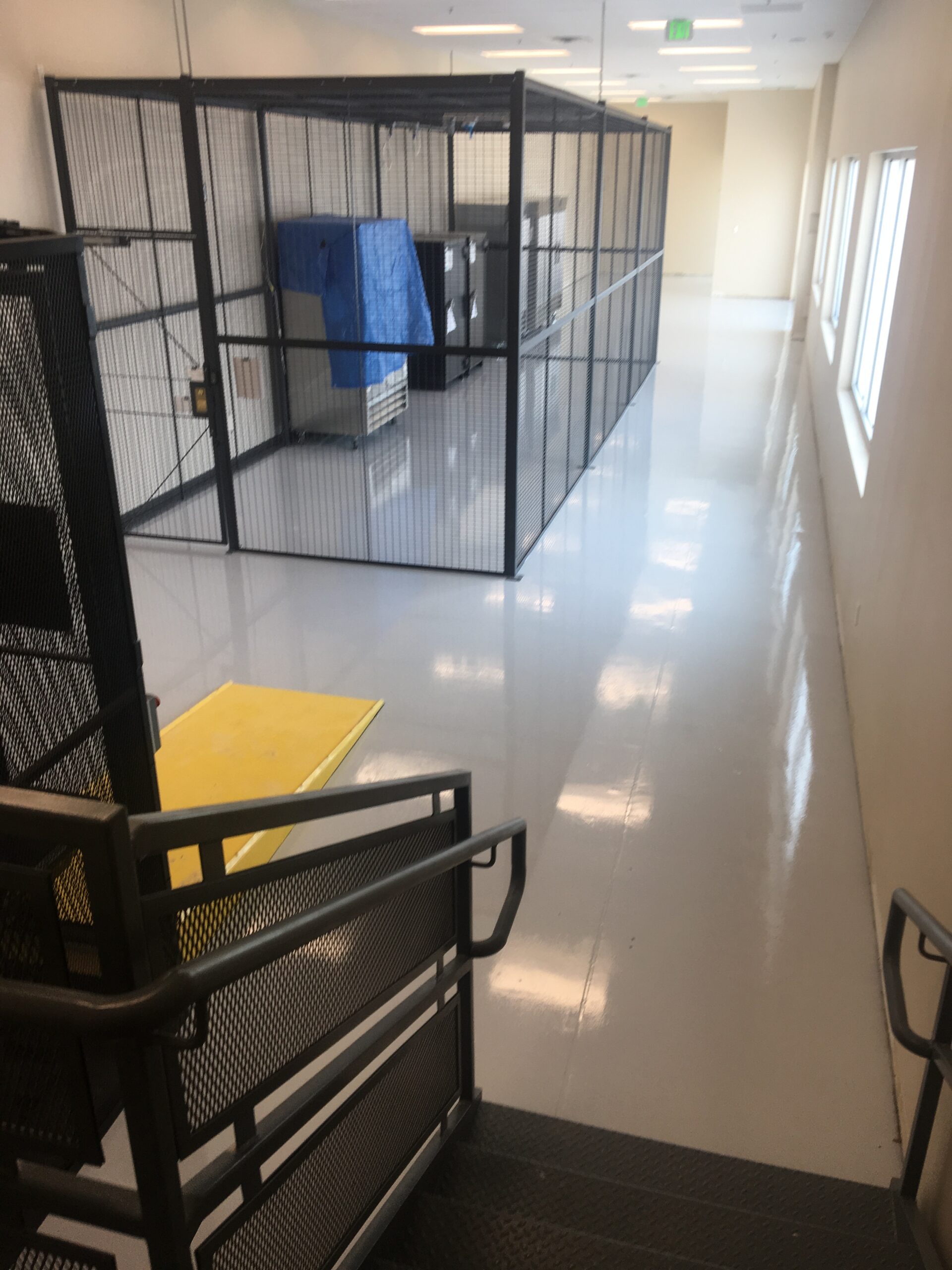 Epoxy floor in a controlled access area with a black fence and yellow mat.