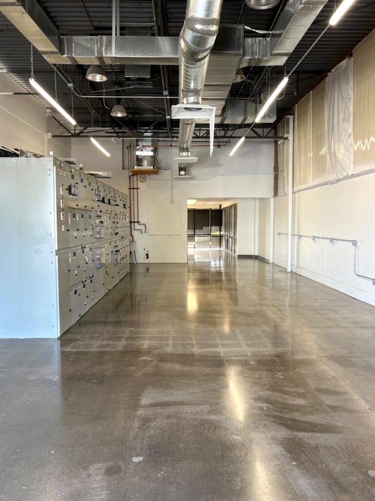 Glossy gray concrete floor in an industrial room lined with electrical switchgear panels