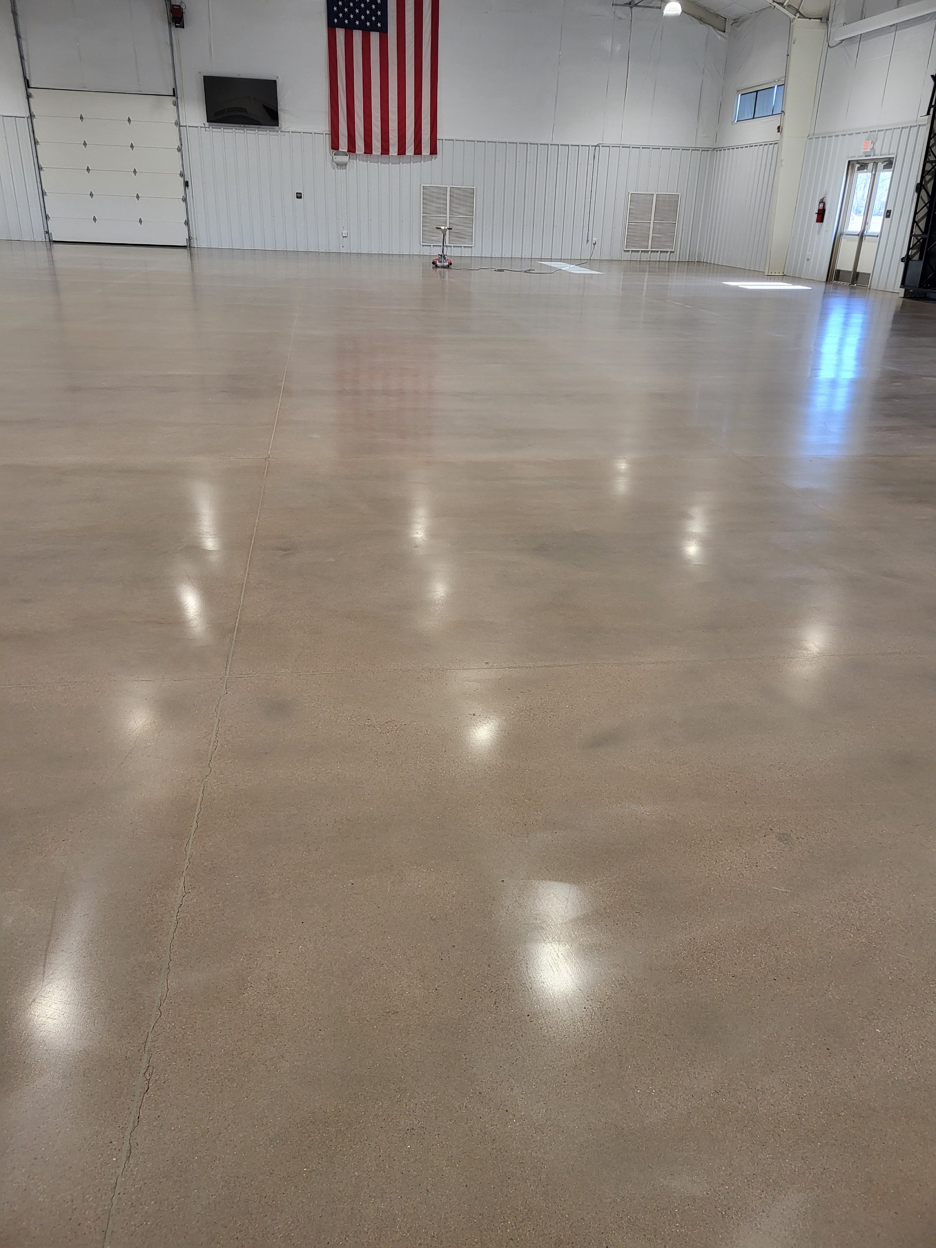 Polished concrete floor in a spacious industrial facility with an American flag in the background.