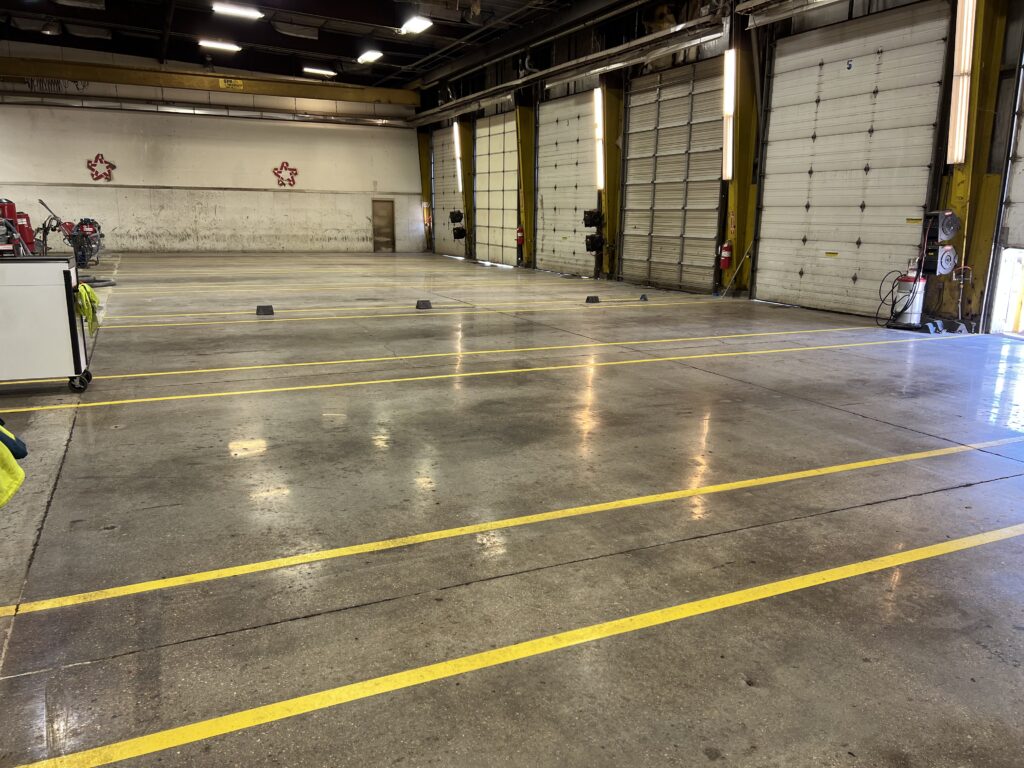 A polished concrete floor with yellow line striping in a large industrial space.