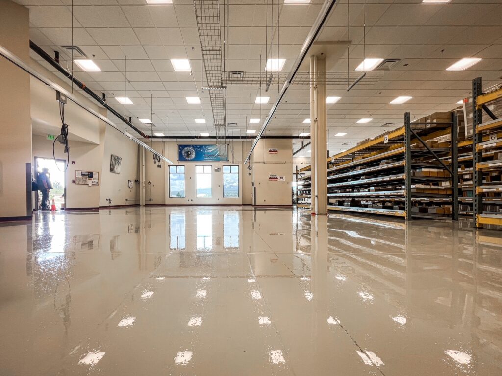 Glossy light gray coated floor in a parts warehouse with stocked shelving racks and a drop ceiling