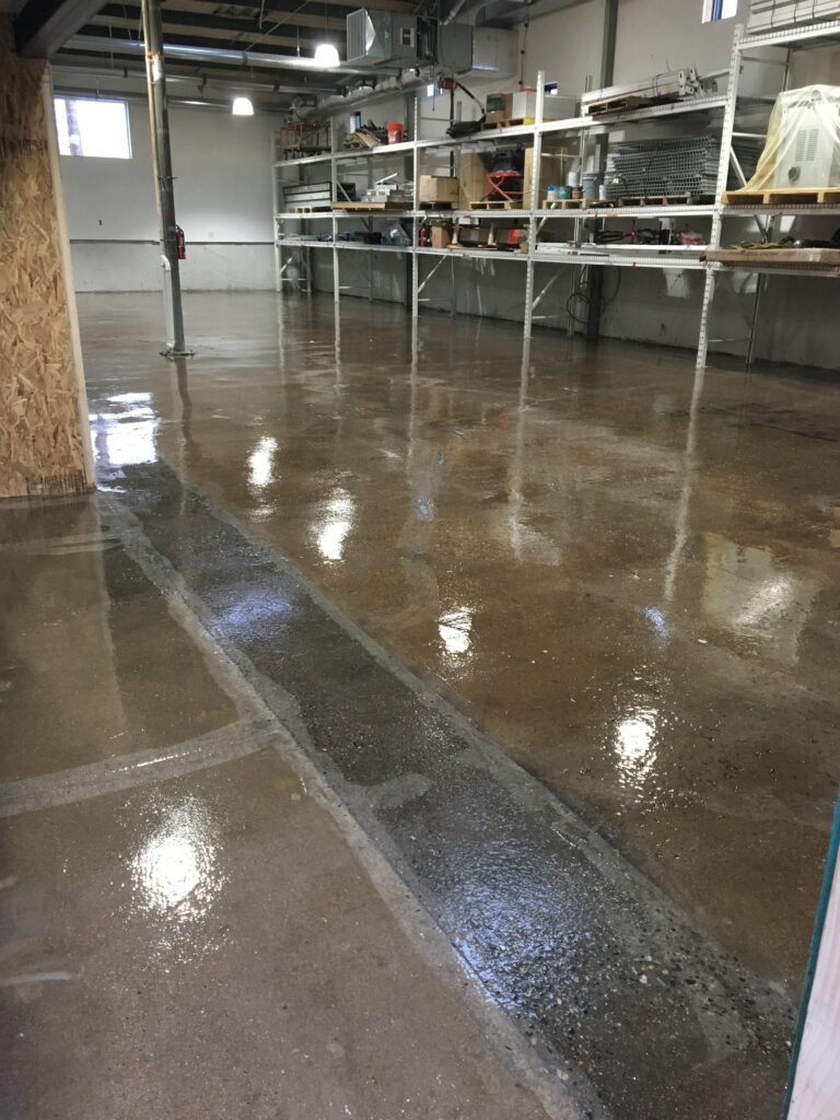 Glossy sealed concrete floor with a repaired trench strip in a workshop with storage shelving