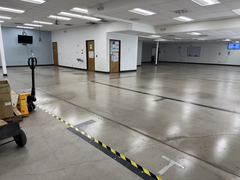 Glossy gray concrete floor in an open commercial workspace with a pallet jack and floor hazard tape.