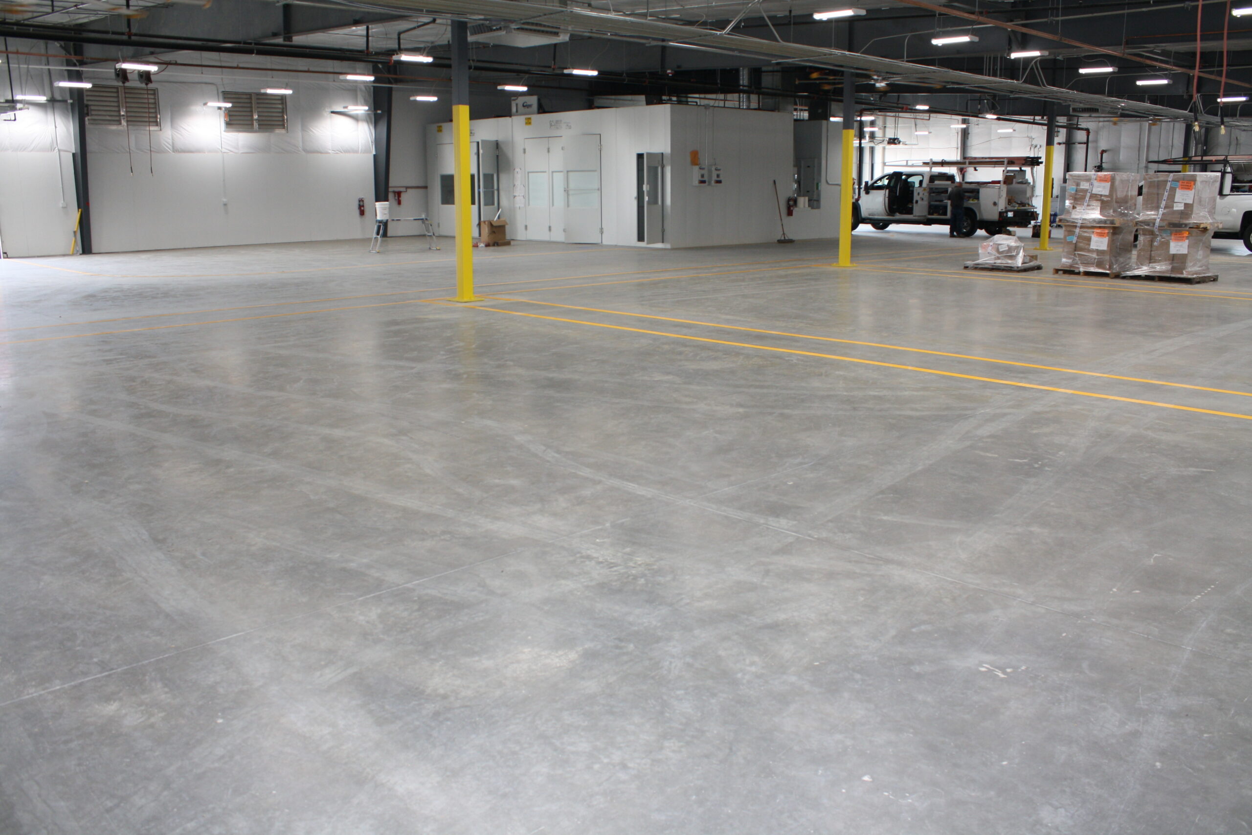 Wide view of a clean warehouse floor with yellow line striping after professional concrete grinding