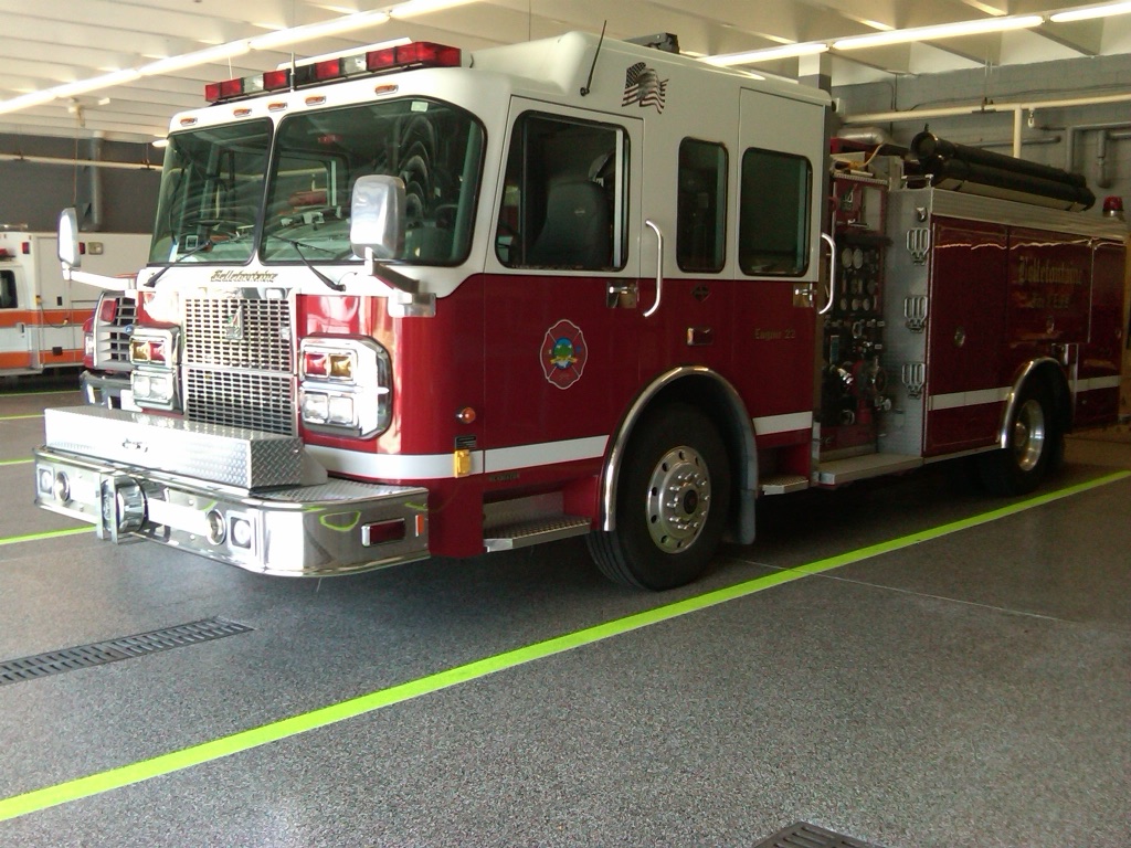 Red fire engine on a gray flake-epoxy floor with safety striping in a fire-station apparatus bay